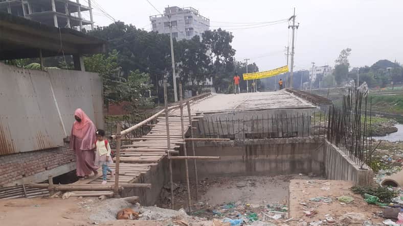 গাজীপুর মহানগরীর কালা শিকদার ঘাটে ২৩ কোটি টাকা ব্যয়ে একটি সেতু নির্মাণের দুই বছর পরও সংযোগ সড়ক না থাকায় সুফল পাচ্ছেন না স্থানীয়রা। বর্তমানে সেতুটি সড়ক থেকে উঁচু হয়ে পড়ায় উঠানামায় বিকল্পভাবে চলতে হচ্ছে স্থানীয়দের। এতে দুর্ভোগ বেড়েছে স্থানীয় বাসিন্দাদের। স্থানীয়রা জানান, জনদুর্ভোগ লাঘবে চিলাই নদীর ওপর এ সেতুটি নির্মাণ করে গাজীপুর সিটি কর্পোরেশন। সেতুর দক্ষিণ পাশে গাজীপুর শহরের অফিস আদালত, উত্তরে ২৫নং ওয়ার্ড ভুরুলিয়াসহ একাধিক গ্রাম। সেতুটিতে দুই পাশে সংযোগ না থাকায় সাঁকো বেয়ে সেতুর ওপরে উঠে চলাচল করতে হয় এলাকাবাসীর। ভুরুলিয়া গ্রামের স্কুল শিক্ষার্থী আল-আমিন বলেন, প্রতিদিন জেলা শহরের বিদ্যালয়ে যেতে এই সেতু পার হতে কষ্ট হয়। আমার মতো এলাকার প্রত্যেকটা শিক্ষার্থীর একই অবস্থা। সেতু হওয়ার পরও আমাদের বাঁশ কাঠ দিয়ে পার হতে হয়। এখানে বাইসাইকেল, রিকশা-ভ্যান ও মোটরসাইকেল পারাপার করার কোনো সুযোগ নেই। অটোরিকশা চালক আব্দুস সালাম বলেন, এখান থেকে কোর্টে, ডিসি অফিসে যেতে মাত্র দুই তিন মিনিট সময় লাগে। হেঁটে সেতু পার হয়ে রিকশায় উঠতে হয়। সেতু পার হতে গিয়ে কয়েকজনের হাত-পা ভাঙার ঘটনা ঘটেছে। গাজীপুর আদালতের আইনজীবী হাবিুবর রহমান বলেন, ভুরুলিয়া থেকে হেঁটে এসে কাঠের সাঁকো দিয়ে খুব কষ্টে সেতু পার হয়ে এসে রিকশায় উঠতে হয়। বিশেষ করে বৃষ্টির সময় দুর্ভোগ আরও বেড়ে যায়। এই সেতু দিয়ে অনেক মানুষ যাতায়াত করে। দেখার কেউ নেই। কিছু দিন আগে একবার উদ্যোগ নিয়ে আর সংযোগ দেওয়া হয়নি। এই সেতুর দুপাশে সংযোগ সড়কের কাজ করা জরুরি গাজীপুর সিটি কর্পোরেশন ২৫ নং ওয়ার্ড কাউন্সিলর মজিবুর রহমান বলেন, এই সেতুটি নির্মাণ হলেও দুইপাশে সংযোগ দেওয়া হচ্ছে না। ঠিকাদারি প্রতিষ্ঠান এটা নিয়ে গড়িমসি করছে। এতে এলাকাবাসী ও শিক্ষার্থীদের যাতায়াতে সমস্যা হচ্ছে। সামনে বর্ষাকাল তাই দ্রুত সংযোগ দেওয়া প্রয়োজন। এ বিষয়ে গাজীপুর সিটি কর্পোরেশনের নির্বাহী কৌশলী এস এম শামসুর রহমান মাহমুদ বলেন, ২০২০-২০২২ অর্থ বছরের সিটি কর্পোরেশন বিশেষ বরাদ্দে সেতু নির্মাণ শীর্ষক প্রকল্পের আওতায় ২৩ কোটি টাকা ব্যয়ে এই সেতুটি নির্মাণ কাজ শুরু হয়। যার কাজ পুরোপুরি শেষ হয়নি। তিনি বলেন, ঠিকাদারের গাফিলতিতে সেতুটি কাজ শেষ হচ্ছে না। সেতুর দুপাশের সড়কে সংযোগ দেওয়া হয়নি। দ্রুত কাজ শেষ করে সড়কের সংযোগ দিতে ইতোমধ্যেই সংশ্লিষ্ট ঠিকাদারকে চিঠি দেওয়া হয়েছে।